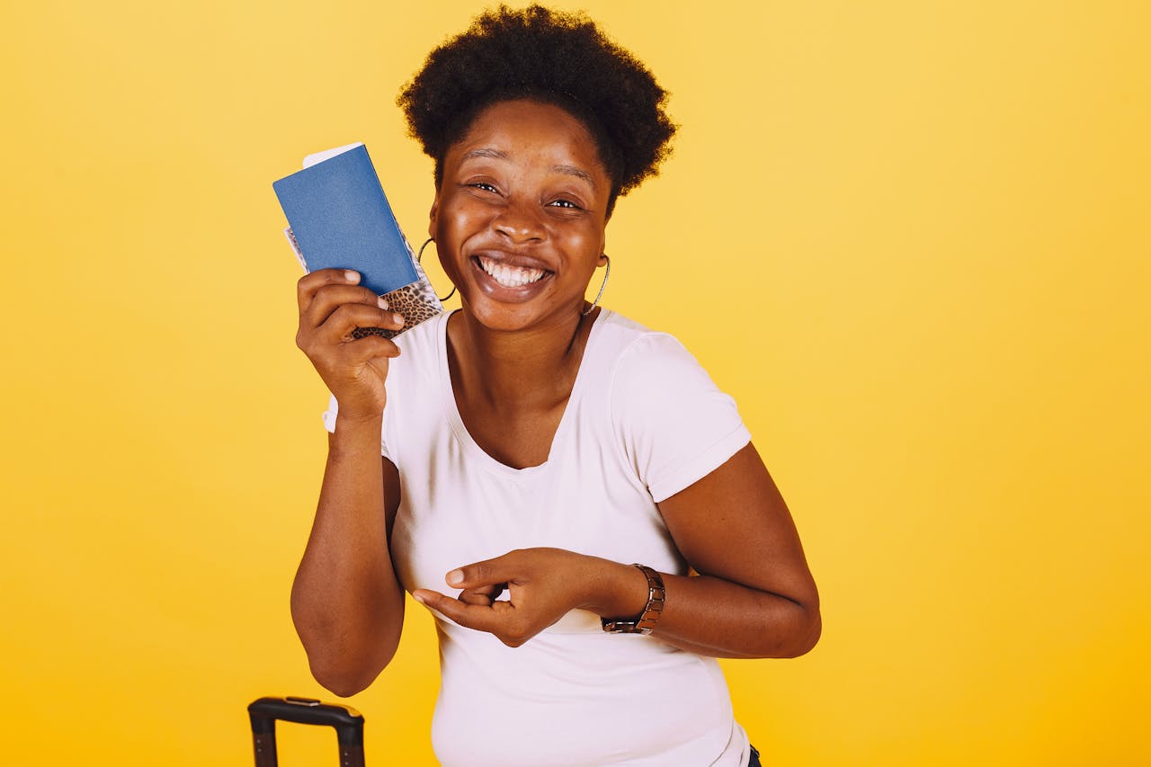 Smiling woman holding passport, ready for vacation on a bright yellow background.